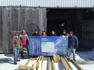 Photo of volunteers holding beside a new billboard, with materials to build a frame for it